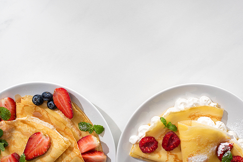 top view of tasty crepes with berries on plates on grey background