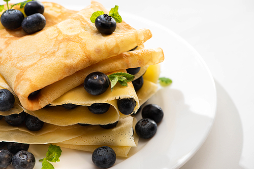 close up view of tasty crepes with mint and blueberries on plate on white background