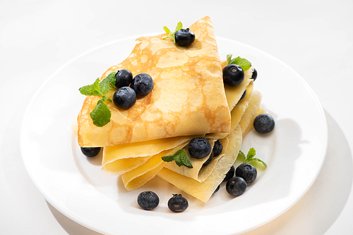 tasty crepes with mint and blueberries on plate on white background