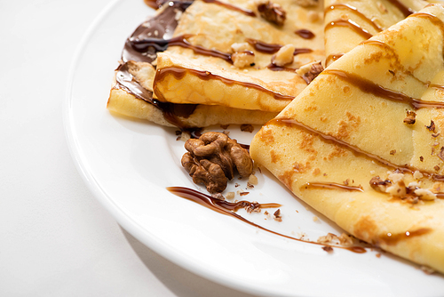 close up view of tasty crepes with chocolate spread and walnuts on plate on white background