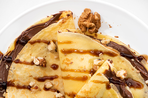 top view of tasty crepes with chocolate spread and walnuts on plate on white background