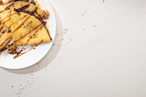 top view of tasty crepes with chocolate spread and walnuts on plate on grey background