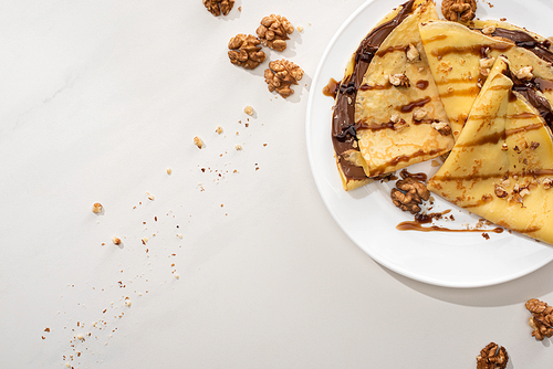top view of tasty crepes with chocolate spread and walnuts on plate on grey background