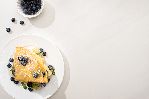 top view of tasty crepes near bowl of blueberries on grey background