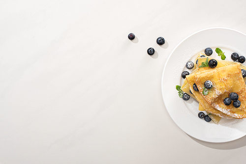 top view of tasty crepes with blueberries and mint on plate on grey background