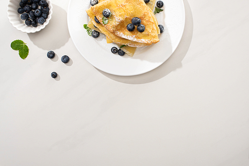 top view of tasty crepes with blueberries and mint on plate on grey background