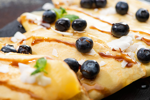 close up view of tasty crepes with blueberries, mint and coconut flakes