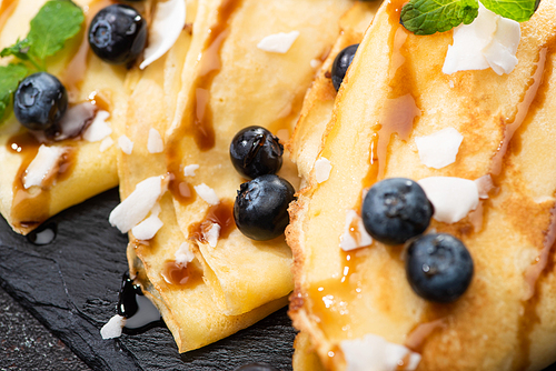 close up view of tasty crepes with blueberries, mint and coconut flakes