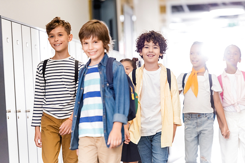 selective focus of multicultural classmates walking along corridor in school