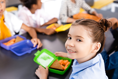 selective focus of schoolgirl  near lunch box with sandwich and fresh carrots