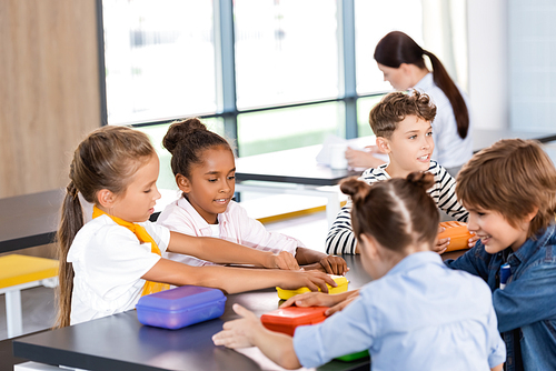 selective focus of multiethnic classmates sitting in school canteen near lunch boxes