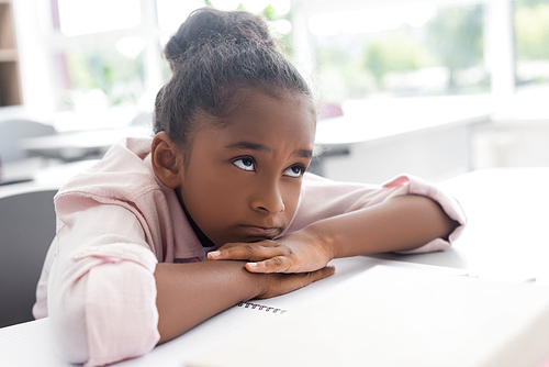 bored african american schoolgirl sitting at desk with head on hands during lesson