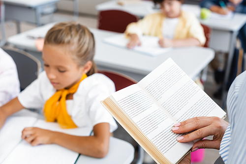 cropped view of teacher reading book near pupils in classroom