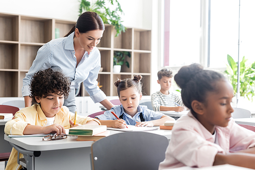 Selective focus of teacher standing near multiethnic pupils during lesson in school