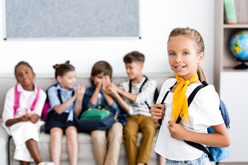 Selective focus of schoolgirl with backpack  with multiethnic friends at background in school