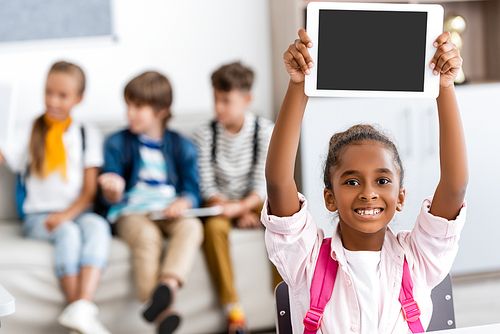 Selective focus of african american schoolgirl holding digital tablet with blank screen in classroom