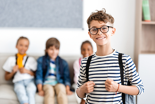Selective focus of schoolboy with backpack and eyeglasses  with classmates at background