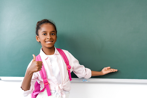 Selective focus of african american schoolgirl showing like gesture and pointing with hand at chalkboard