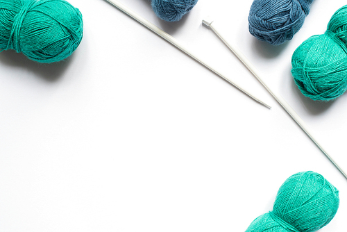 top view of blue and green wool yarn and knitting needles on white background