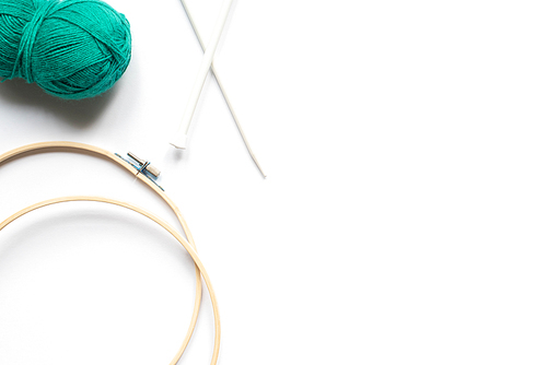 top view of green wool yarn, knitting looms and knitting needles on white background