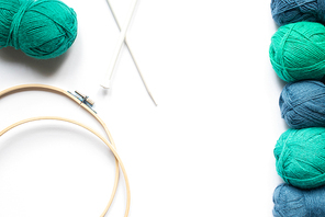 top view of blue and green wool yarn, knitting looms and knitting needles on white background