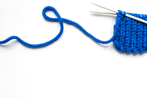 top view of blue wool yarn and knitting needles on white background