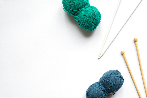 top view of blue and green wool yarn and knitting needles on white background
