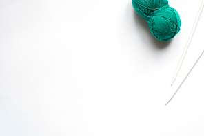 top view of green wool yarn and knitting needles on white background