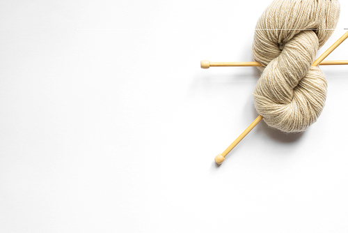 top view of beige wool yarn and knitting needles on white background