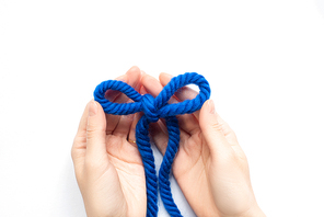 partial view of woman holding bow of blue wool thread on white background