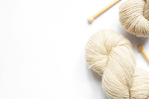 beige yarn and knitting needles on white background with copy space