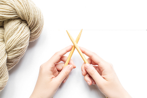 top view of female hands with beige yarn and knitting needles on white background