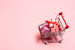 high angle view of toy shopping cart with presents on pink, black friday concept