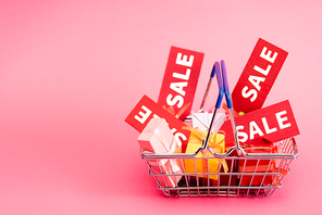 shopping basket with presents and red sale tags on pink