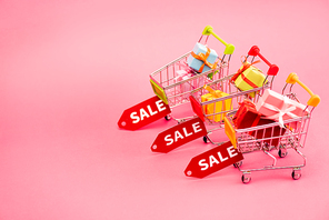 colorful gifts in shopping carts with sale tags on pink, black friday concept