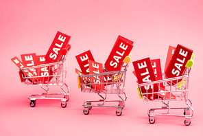 red tags with sale lettering in shopping carts on pink