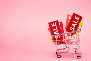 red labels with black friday sale lettering in shopping trolley on pink