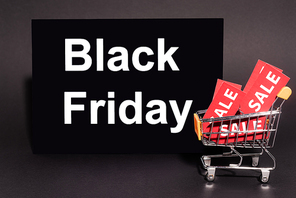 placard with black friday lettering near toy cart with sale tags on dark background