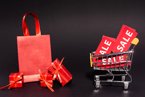 shopping bag and gifts near toy cart with sale tags on dark background, black friday concept