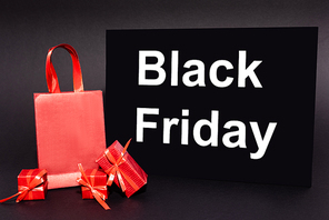 red presents and shopping bag near placard with black friday lettering on dark background