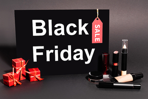placard with black friday lettering and gifts near decorative cosmetics on dark background