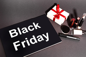 high angle view of placard with black friday lettering and gift near decorative cosmetics on dark background