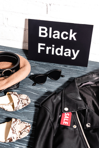shoes, sunglasses, beret and belt near board with black friday and tag with sale lettering on leather jacket