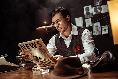 Concentrated detective in glasses reading newspaper in dark office