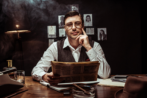 Concentrated detective in glasses reading newspaper in dark office