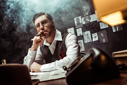 Low angle view of pensive detective in glasses smoking cigar in office