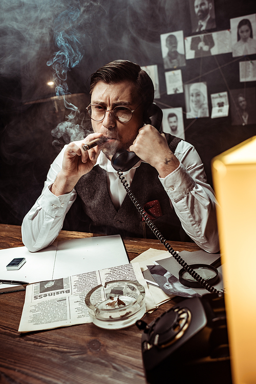 Pensive detective in glasses talking on telephone in dark office