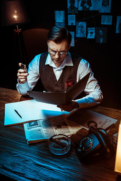 High angle view of concentrated detective in glasses reading dossier in dark office