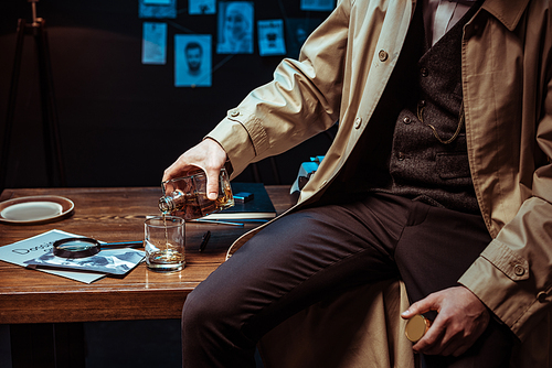 Partial view of detective pouring cognac in glass while sitting on table