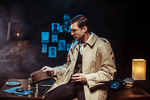 Detective in trench coat sitting on table with hat and glass of cognac